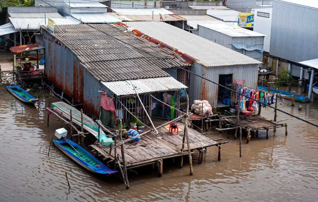 Bateau traditionnel naviguant sur un canal du delta avec maisons sur pilotis et végétation riveraine