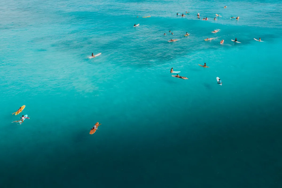 Surfeur pagayant vers une vague de reef break dans une eau turquoise sous un ciel tropical