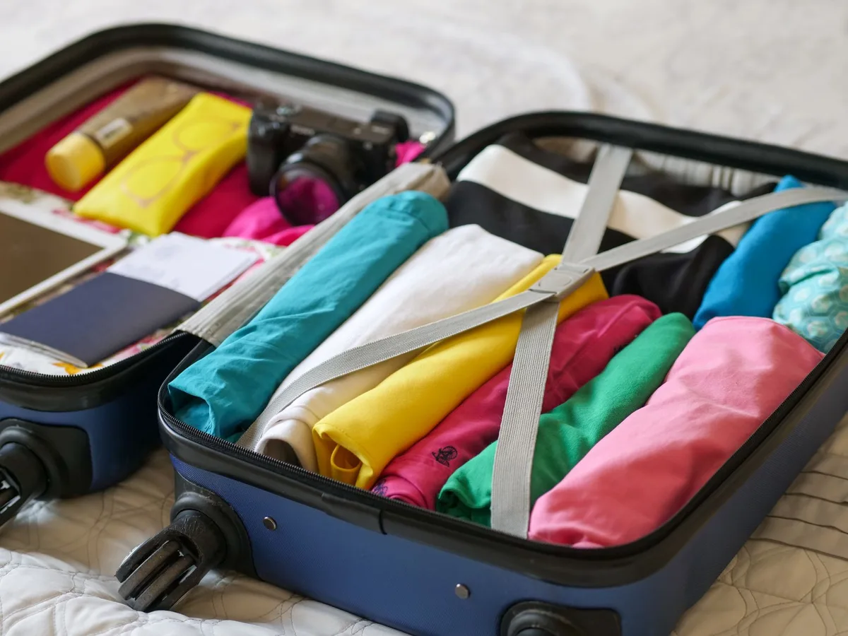 Sac weekender ouvert rempli de vêtements pliés et d'accessoires de voyage, avec une main réglant les sangles