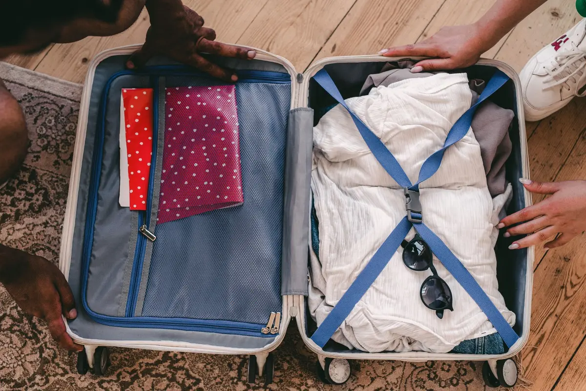 Valise rigide ouverte à l'aéroport avec objets électroniques et souvenirs, mains anonymes, ambiance terminale