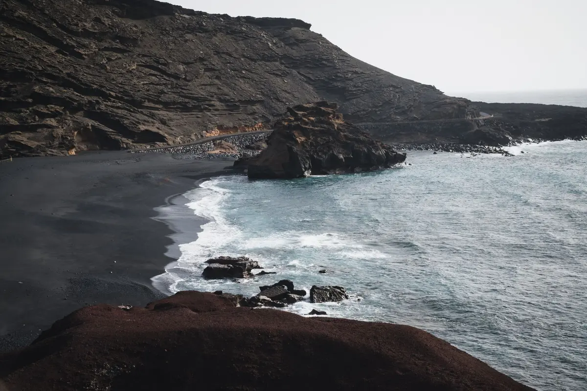 Plage aux sables noirs volcaniques bordée par des falaises rouges et eau turquoise