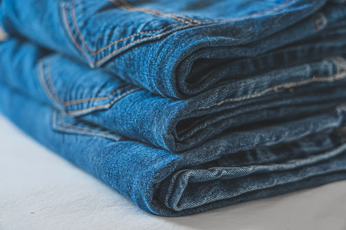 Jeans avec ourlet brut effiloché soigneusement pliés à côté d'un pull et de baskets