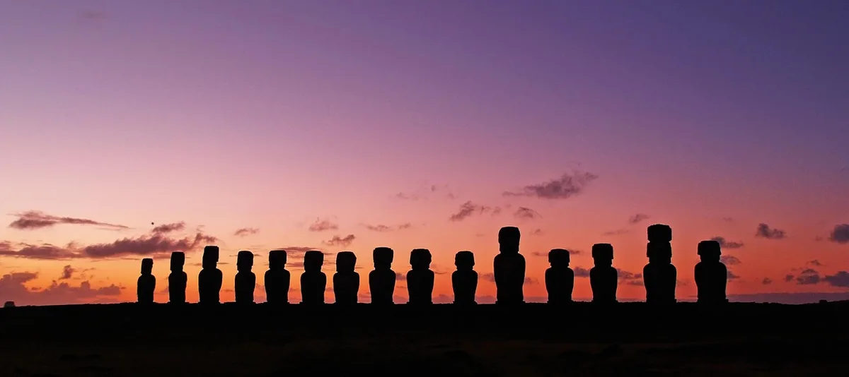 Silhouettes de moaï se détachant contre un ciel coloré au lever du soleil