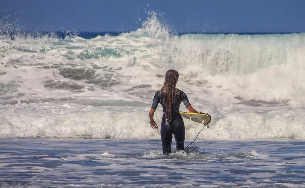 Surfeur pagayant face aux vagues et falaises dorées de l'Algarve au lever du jour