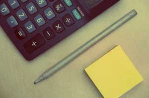 Mains sur un bureau avec carte face cachée, calculatrice et carnet près d'une fenêtre en journée
