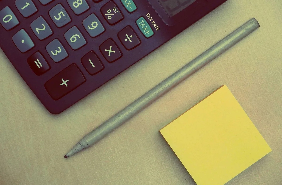 Mains sur un bureau avec carte face cachée, calculatrice et carnet près d'une fenêtre en journée
