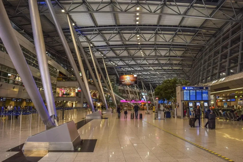 Passants ajustant une valise rigide près d'un tapis roulant d'aéroport en plein jour
